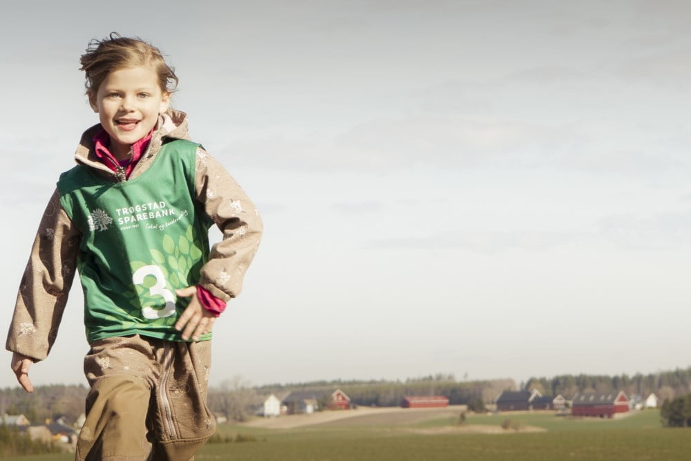 En jente i deltakervest fra Trøgstad Sparebank løper med en gård i bakgrunnen